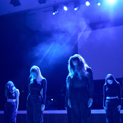 Tänzer der Tanzschule Böhm in schwarzer Kleidung bei einer Bühnenperformance in blauem Licht.