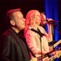 Live-Auftritt der Band mit Sängerin auf der Bühne unter rotem Licht.