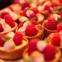 Kleine Törtchen mit Himbeeren und Sahne auf einem Buffet angerichtet.