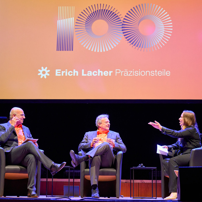 Podiumsgespräch mit drei Personen vor einer Leinwand zum 100-jährigen Jubiläum von Erich Lacher.
