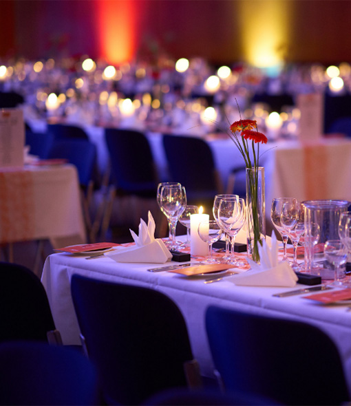 Feierlich gedeckte Tische mit Kerzenlicht und Menüheften im Saal des 100-jährigen Firmenjubiläums.