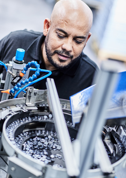 Facharbeiter inspiziert glänzende Drehteile an einer automatisierten Sortieranlage im Produktionsbereich.