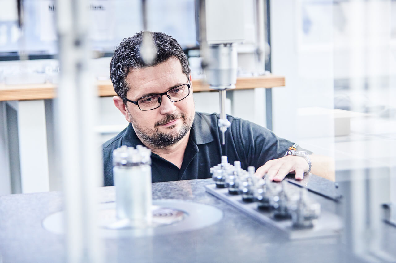 Mitarbeiter überwacht Zuführeinheit mit glänzenden Präzisionsteilen in hochmoderner Fertigungsanlage.
