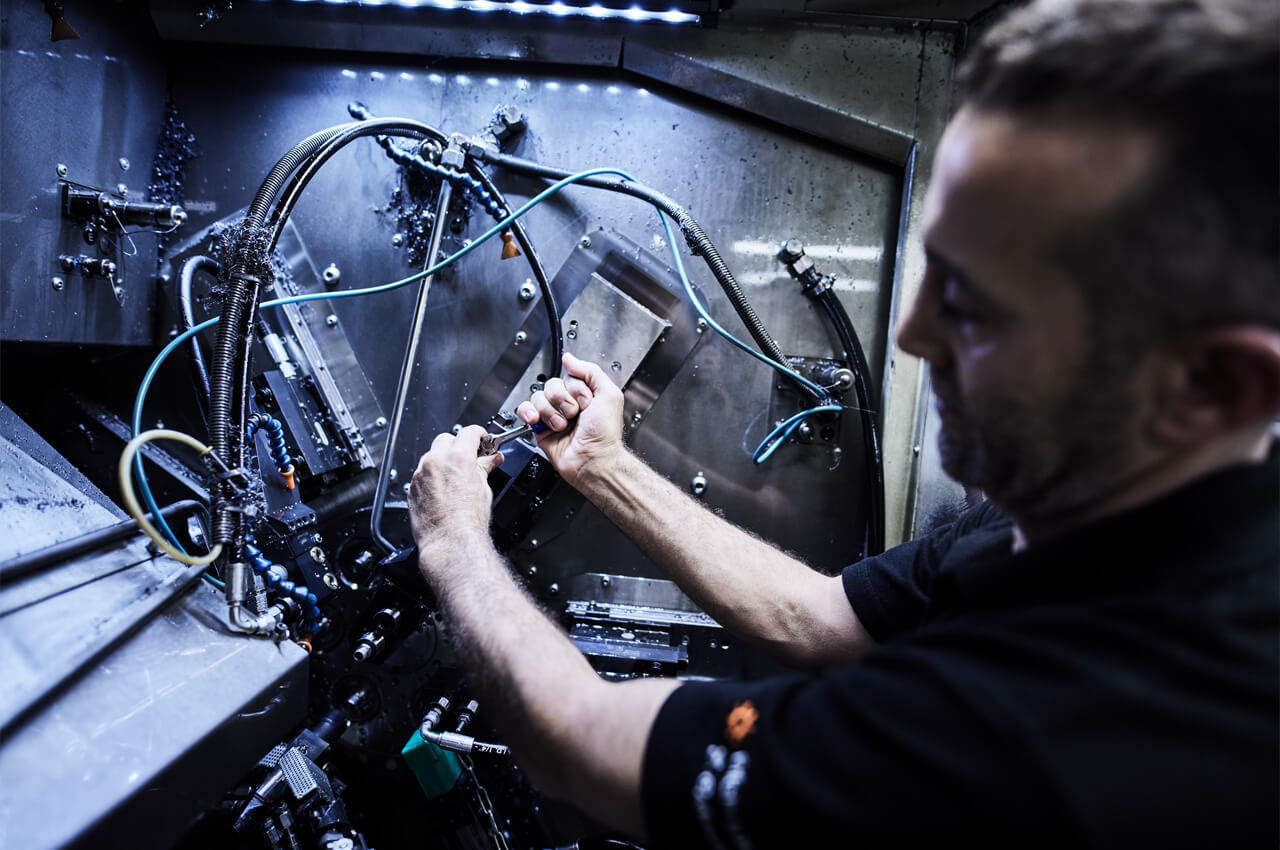 Mitarbeiter führt Feinjustierung an komplexer CNC-Maschine durch.