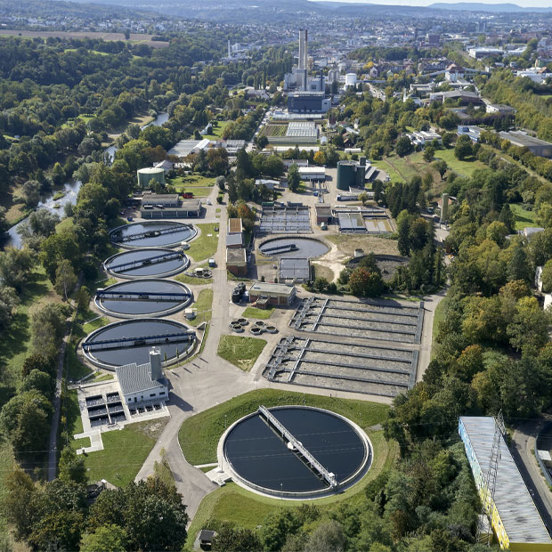 Luftbild einer weitläufigen Kläranlage mit mehreren runden und rechteckigen Becken, eingebettet in grüne Umgebung am Stadtrand von Pforzheim.