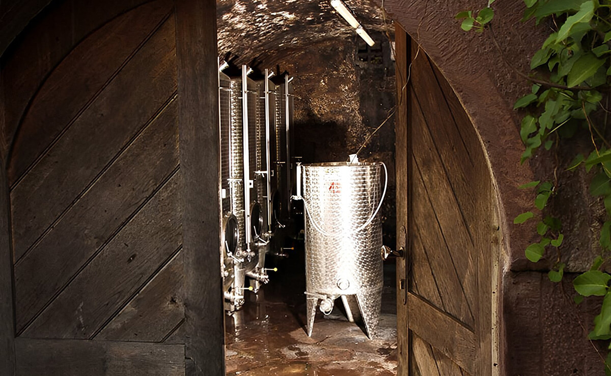 Blick durch geöffnete Holztür in einen Weinkeller mit großen Edelstahltanks.